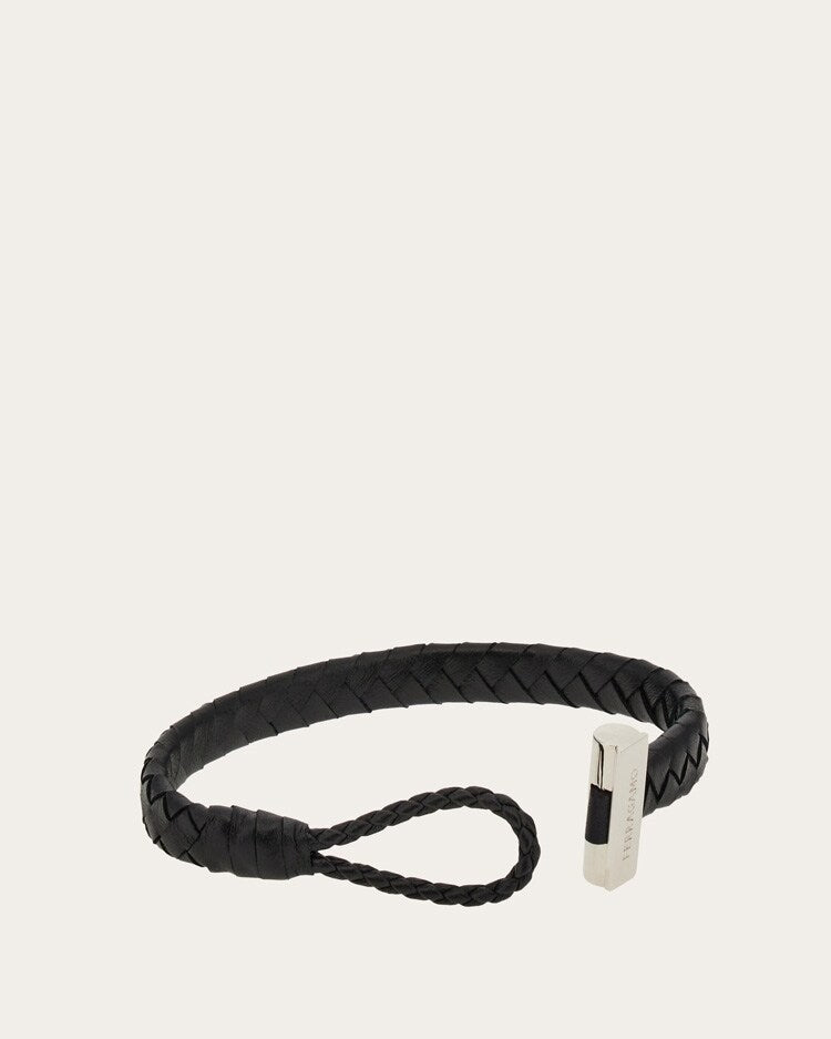 A black braided leather bracelet with a silver-toned rectangular metal accent and a matching braided loop, shown on a plain light beige background.