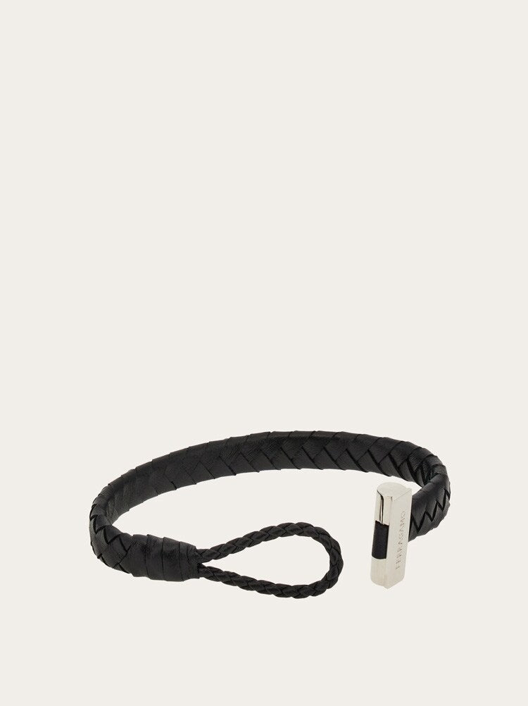 A black braided leather bracelet with a silver-toned rectangular metal accent and a matching braided loop, shown on a plain light beige background.